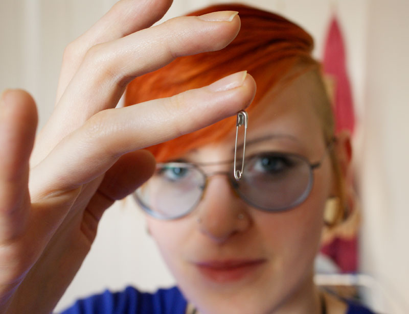 A woman holds up a finger, to which a safety pin is magnetically attracted