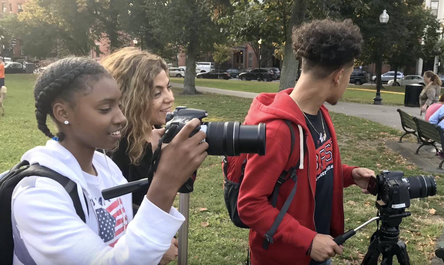 Young people smiling and working with Rashin using cameras in a park