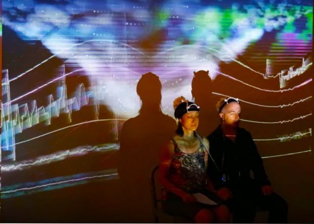 Two people sharing a 3D-printed brain computer interface with projected visuals behind them
