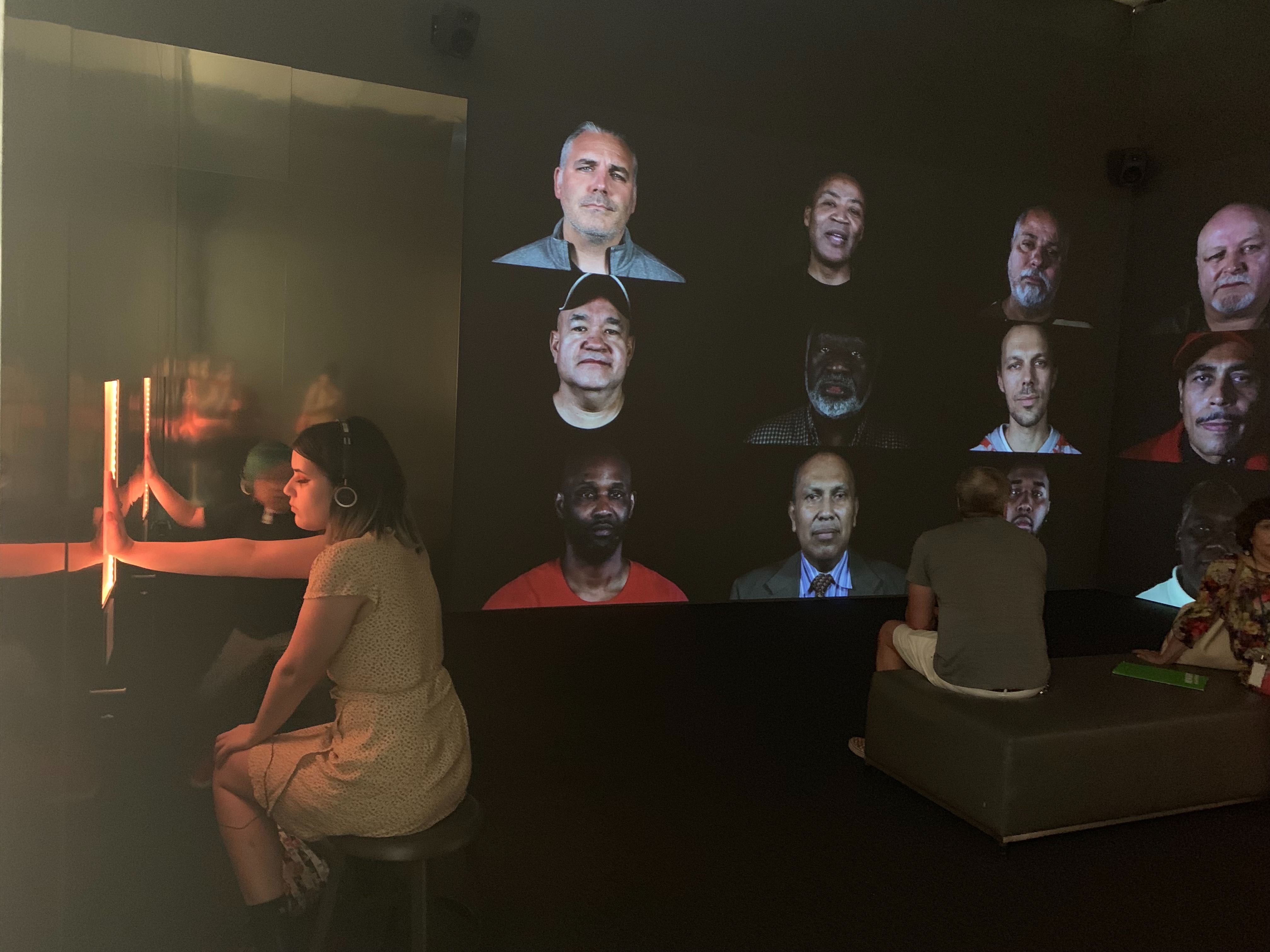 Photo of people sitting in front of projection screens displaying portraits