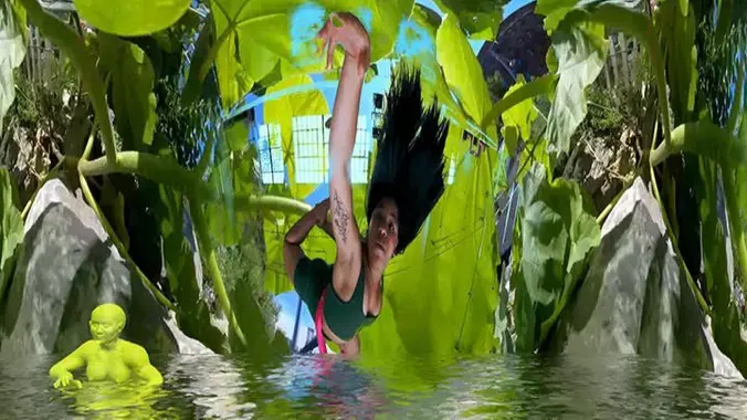 A screenshot with a female dancer hanging upside-down from a ceiling surrounded by foliage, over a virtual water line