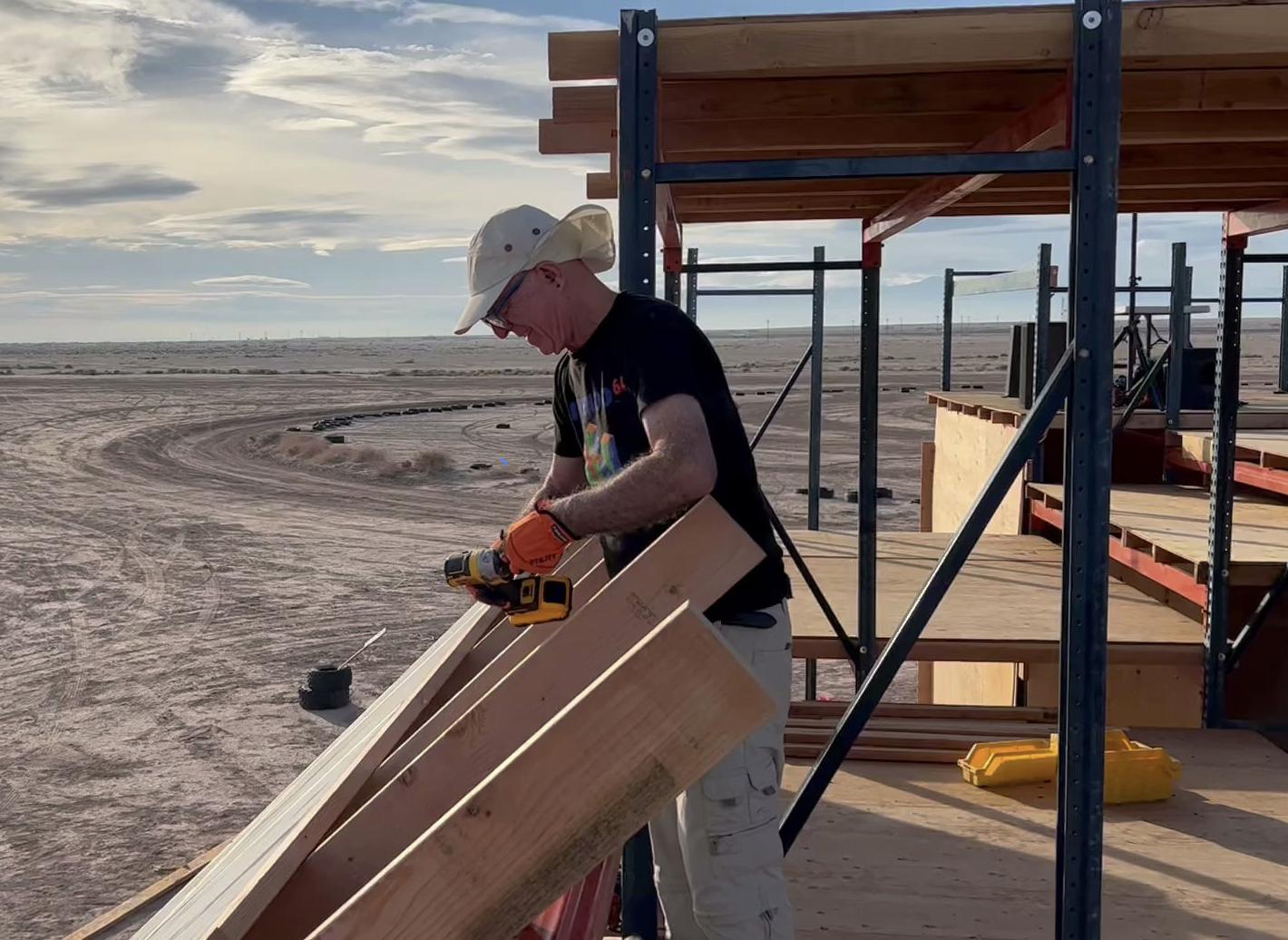 A man using a drill to assemble solar panels to an angled wall in a desert lanscape