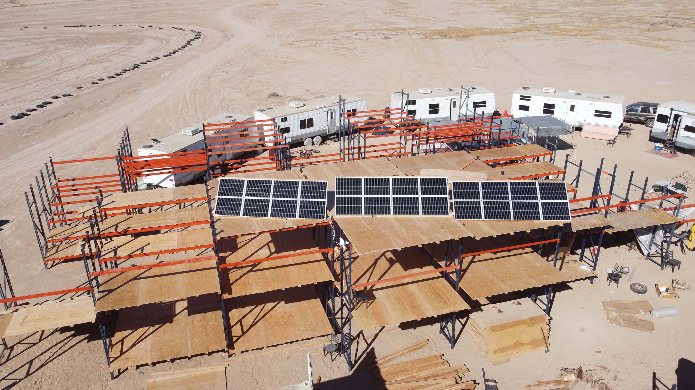 Three large solar panels arranged on top of a large pallet-rack structure in the desert