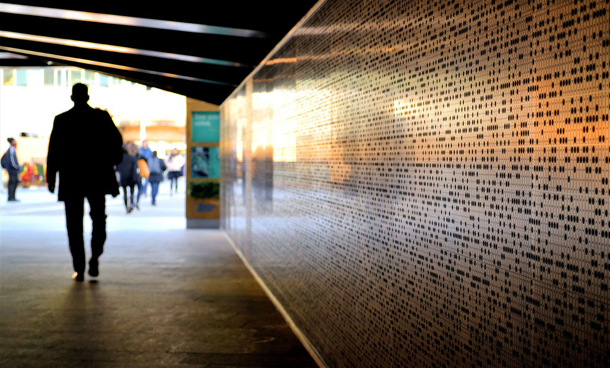A man walks by a wall patterned with lots of tiny black dots