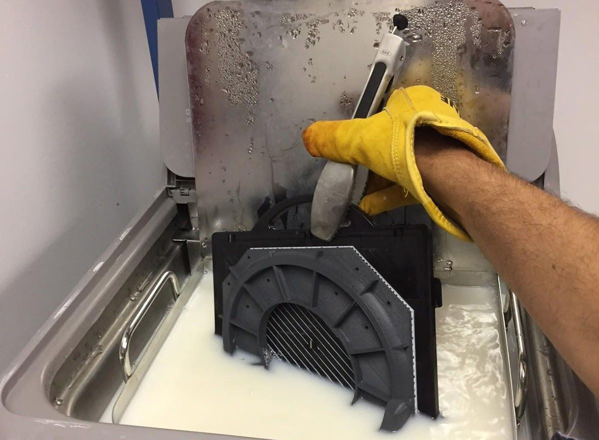 A gloved hand lowers a mold structure into a milky liquid
