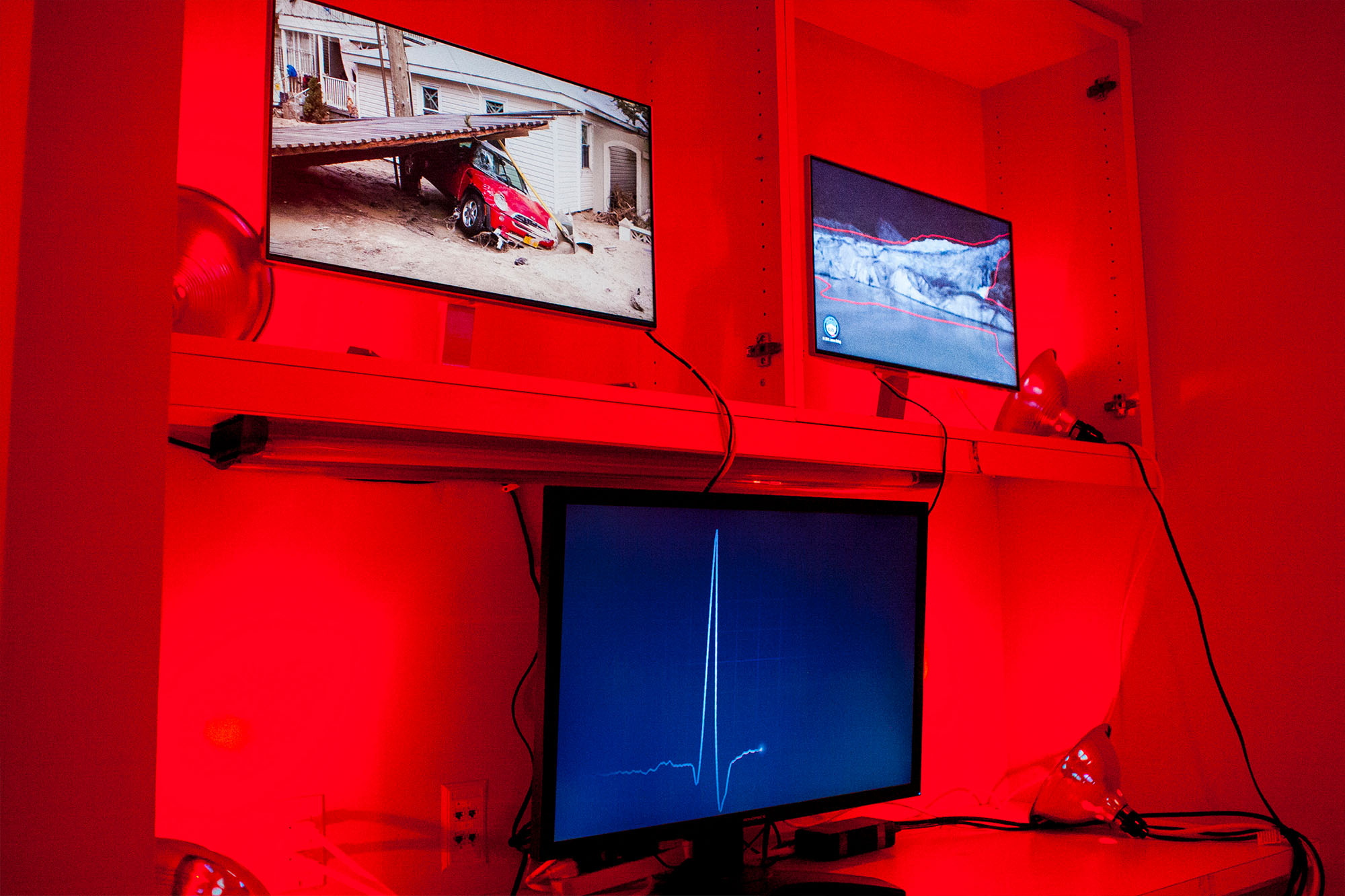 Video screens showing glacial retreat, storms and a heartbeat display in a red lit room
