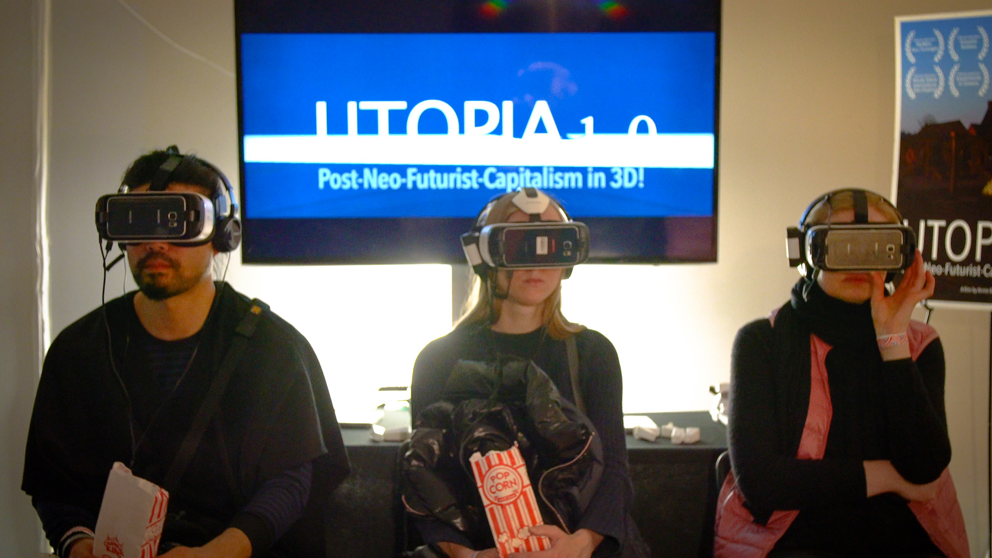 Three particpants wear VR headgear alongside the UTOPIA on screen behind them