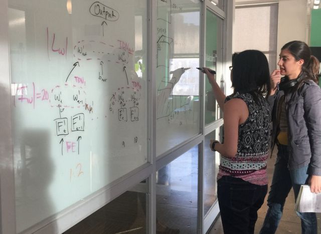 Engineers draw diagrams on a long set of whiteboards