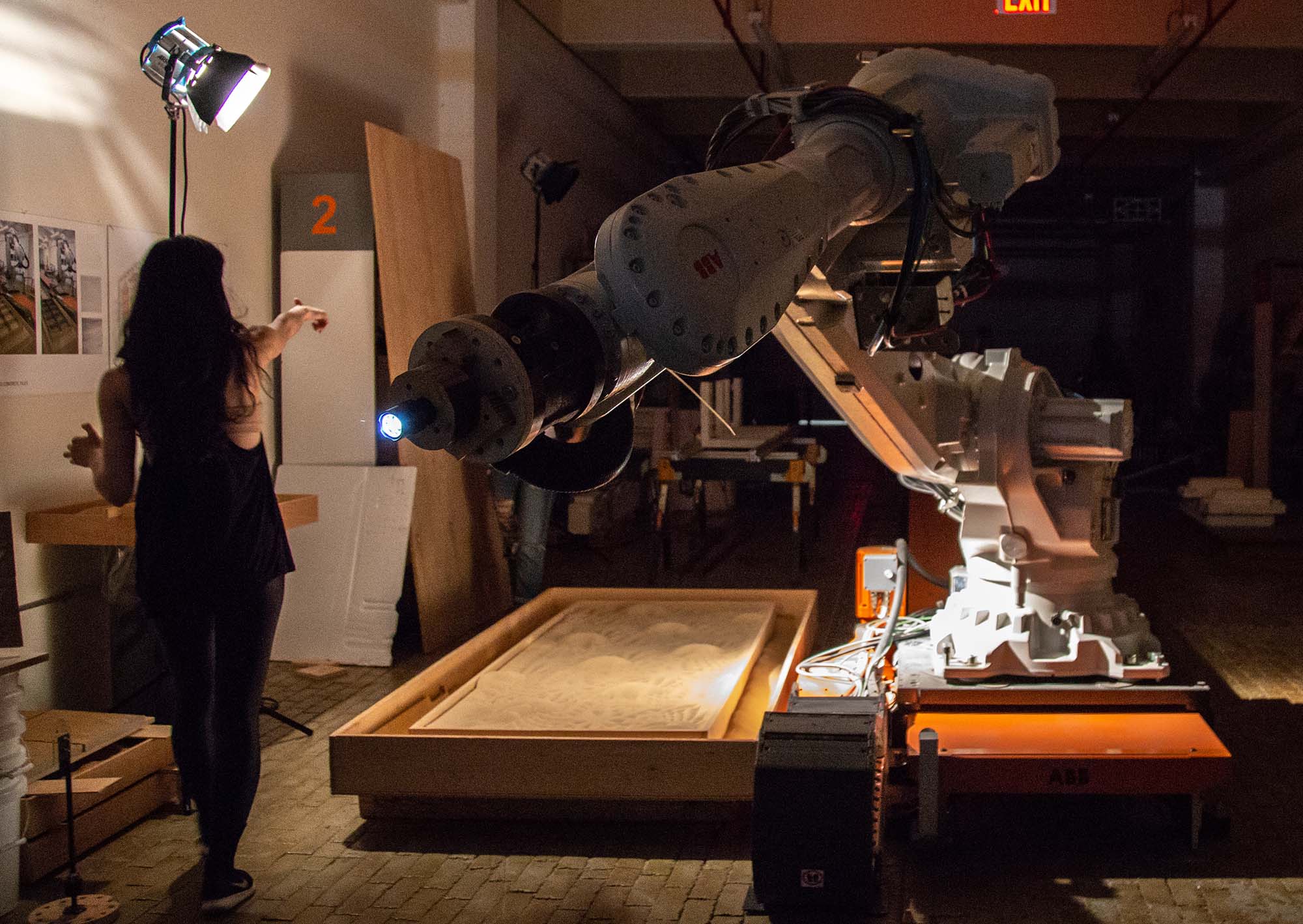 A woman directs an industrial robot arm which is larger than her