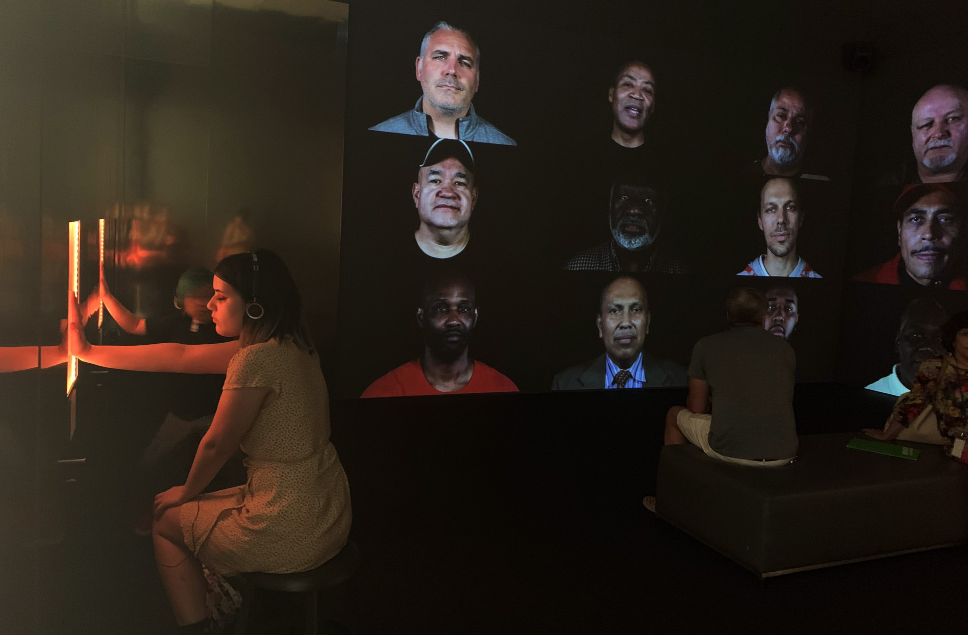 A wide shot of audience members enjoying Rashin’s installation, made up of screens of men singing lullabies