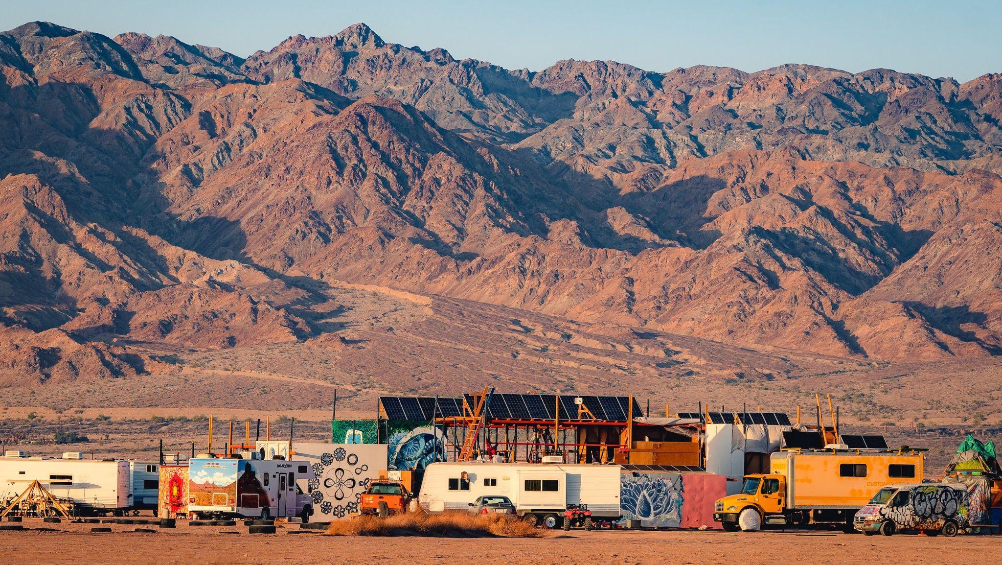 A landscape shot of several caravans set against a large desert mountain backdrop