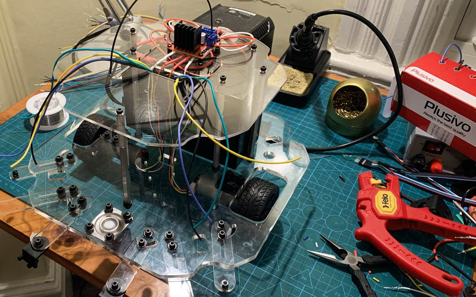 A partially assembled robot with wheel and wires hanging out, alongside soldering tools