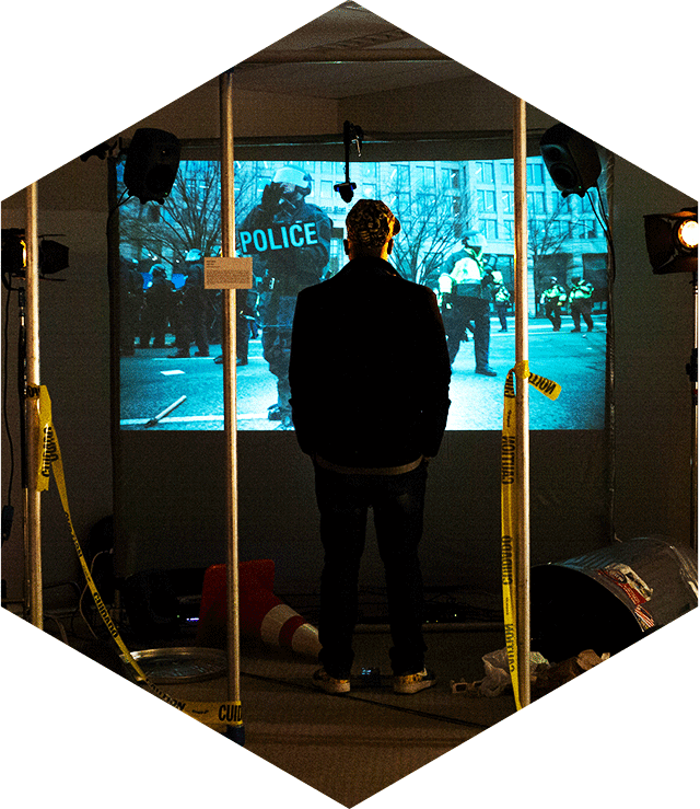 A man seen from behind watching a largw screen with riot police depicted on it